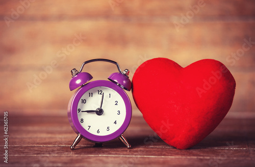 Retro alarm clock and heart shape on wooden table.