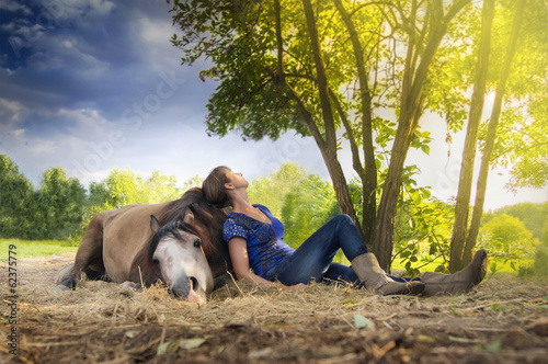 woman resting ,horse lying, outdoors under  tree in sunset