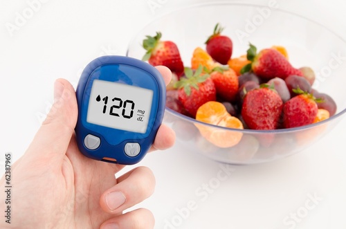 Hand holding meter. Diabetes doing glucose level test. Fruits in