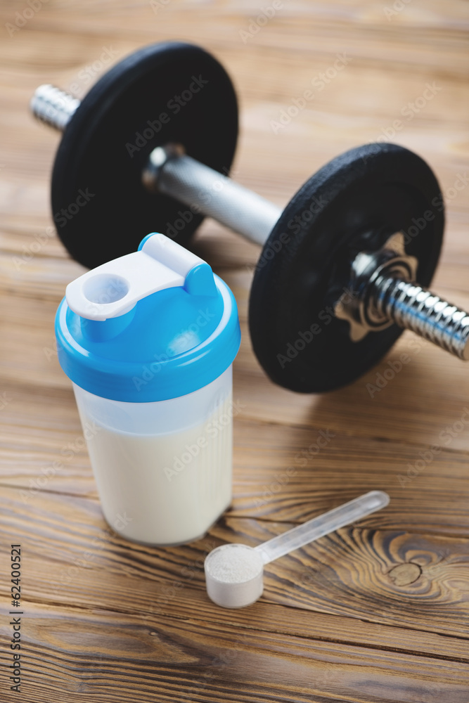 Bodybuilding components: protein shake and a dumbbell, close-up Bodybuilding components: protein shake and a dumbbell, close-up