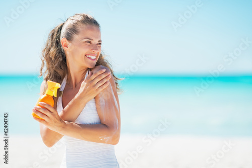 Young woman on beach applying sun block creme and looking on cop