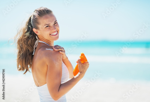 Smiling young woman on beach applying sun block creme