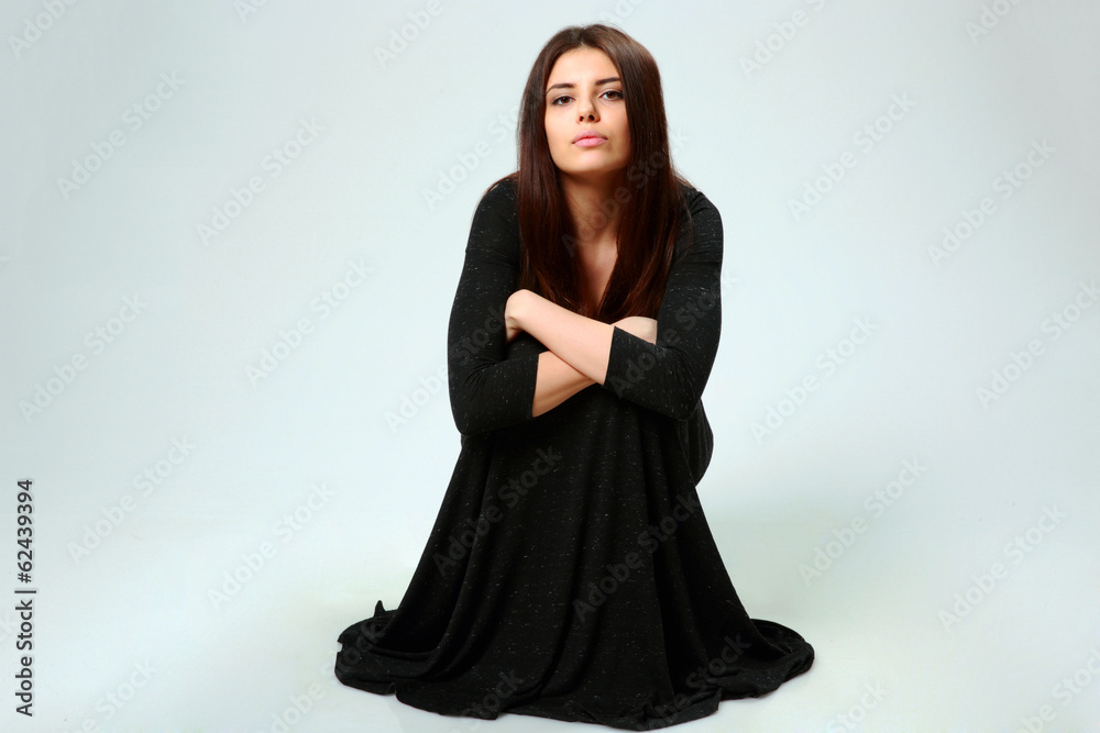 woman in black dress sitting on the floor on gray background woman in black dress sitting on the floor on gray background