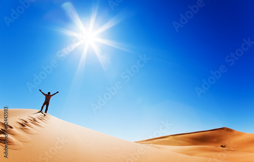 adult white man standing on a sand dune and holding arms up