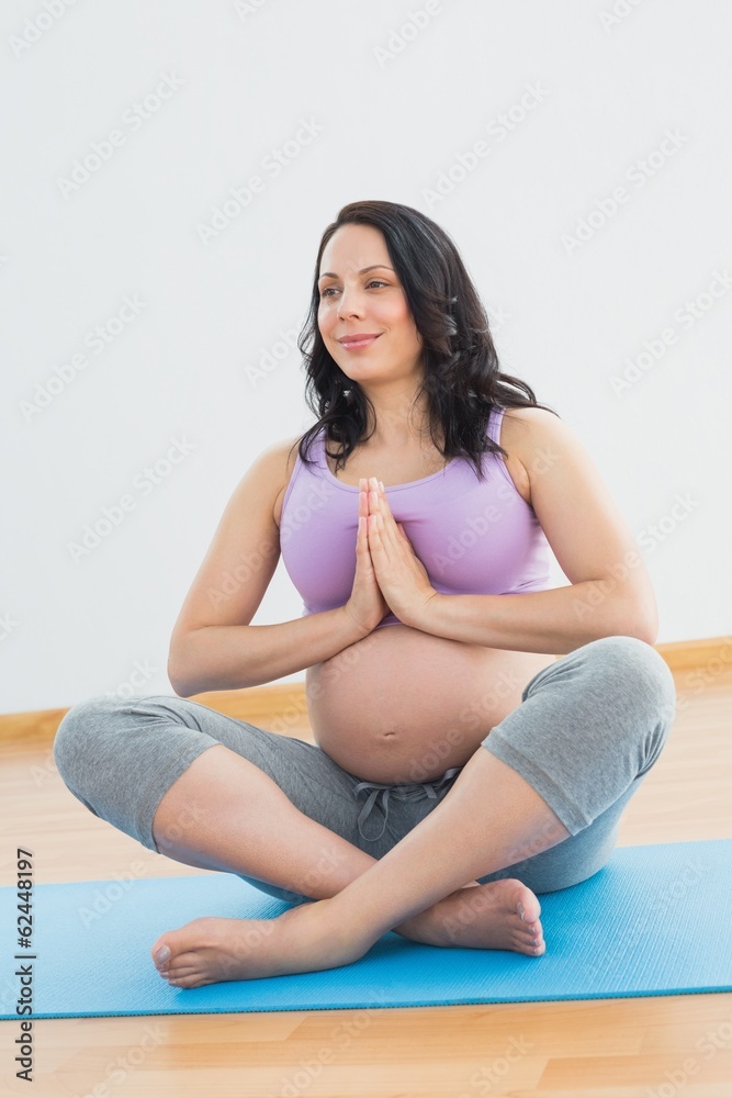 Pregnant woman sitting on mat in lotus pose smiling Pregnant woman sitting on mat in lotus pose smiling