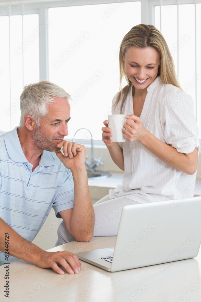 Cheerful couple using laptop together at the counter Cheerful couple using laptop together at the counter