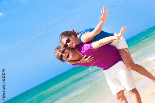 Happy couple in sunglasses on holiday piggybacking cheerful on