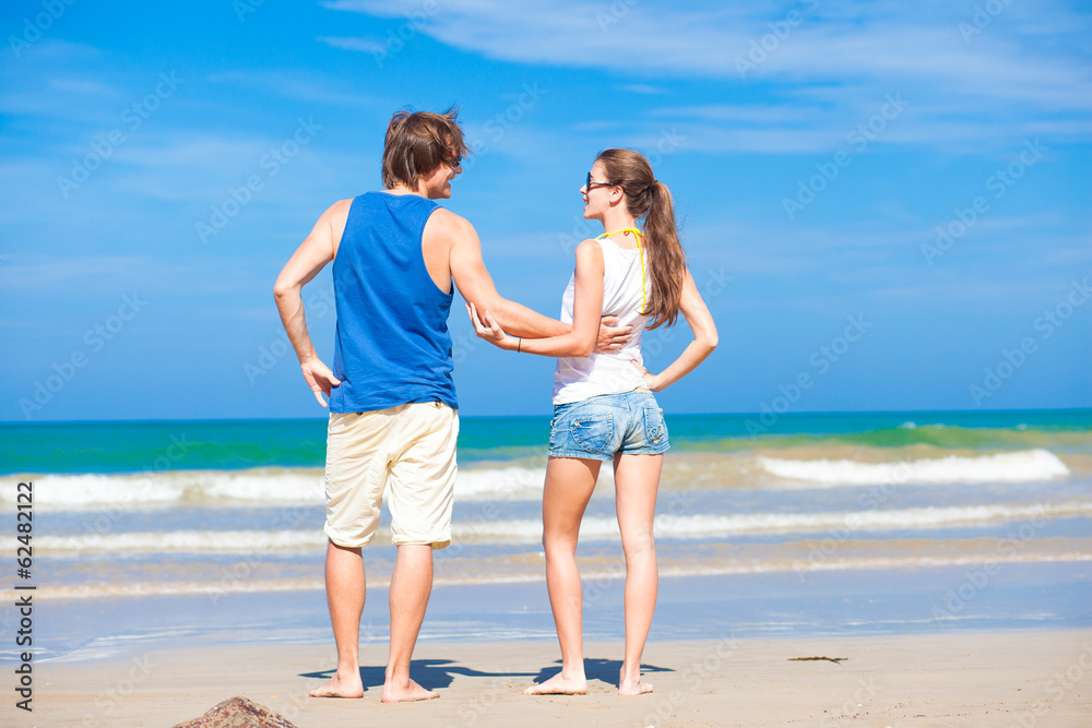 back view of couple flirting on tropical beach in sunglasses in