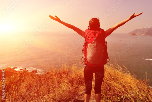 cheering woman hiker open arms at sunrise seaside