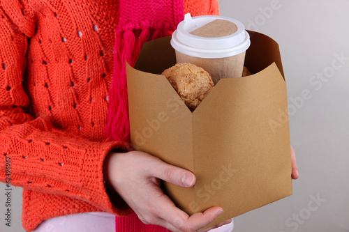 Woman holds box with coffee and cookies on grey background