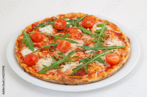 Pizza with tomato and arugula on white plate
