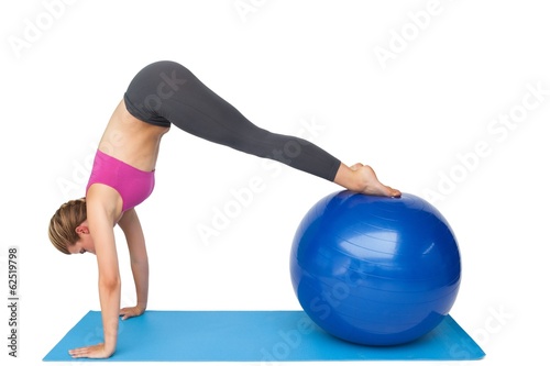 Side view of a fit young woman stretching on fitness ball