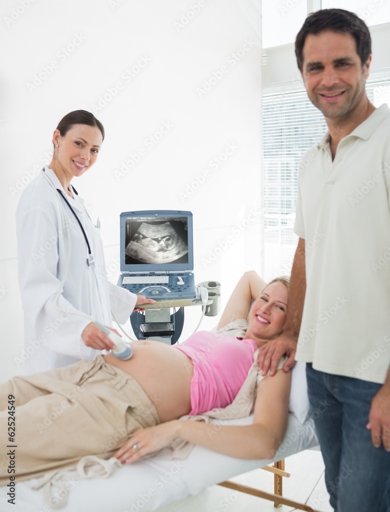Fototapeta premium Expectant couple with doctor performing ultrasound