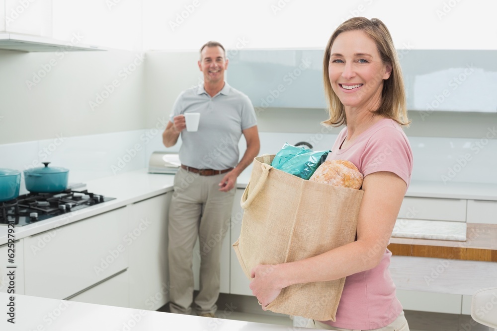Fototapeta premium Woman carrying grocery bag while man with coffee cup in kitchen