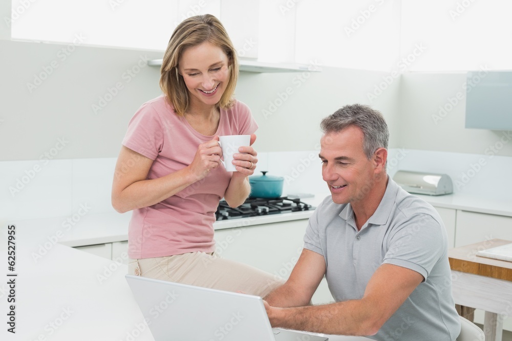 Obraz premium Couple using laptop while woman drinking coffee in kitchen