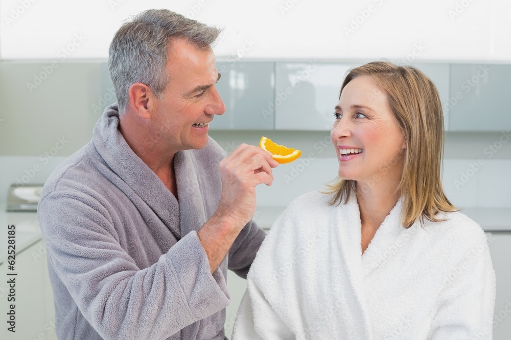 Man feeding woman orange slice in kitchen Man feeding woman orange slice in kitchen