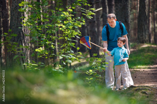 Young father and son catching butterfly in forest photo