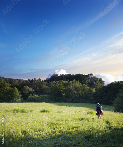 tourist walking on a footpath across the field © vladis_studio