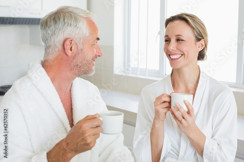 Smiling couple having coffee at breakfast in bathrobes