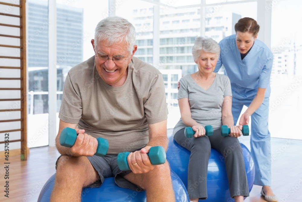 Female therapist assisting senior couple with dumbbells