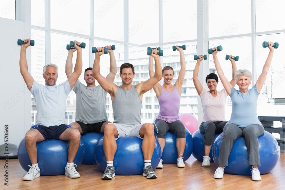 Fitness class with dumbbells sitting on exercise balls in gym Fitness class with dumbbells sitting on exercise balls in gym