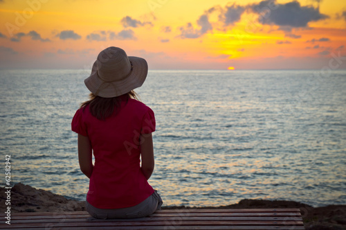 Young woman in hat sitting and looking at sunset