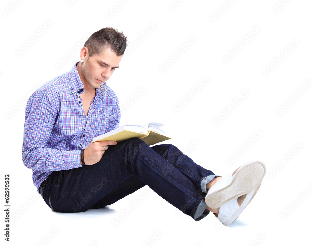 Young man sitting on floor and reading a book isolated on white