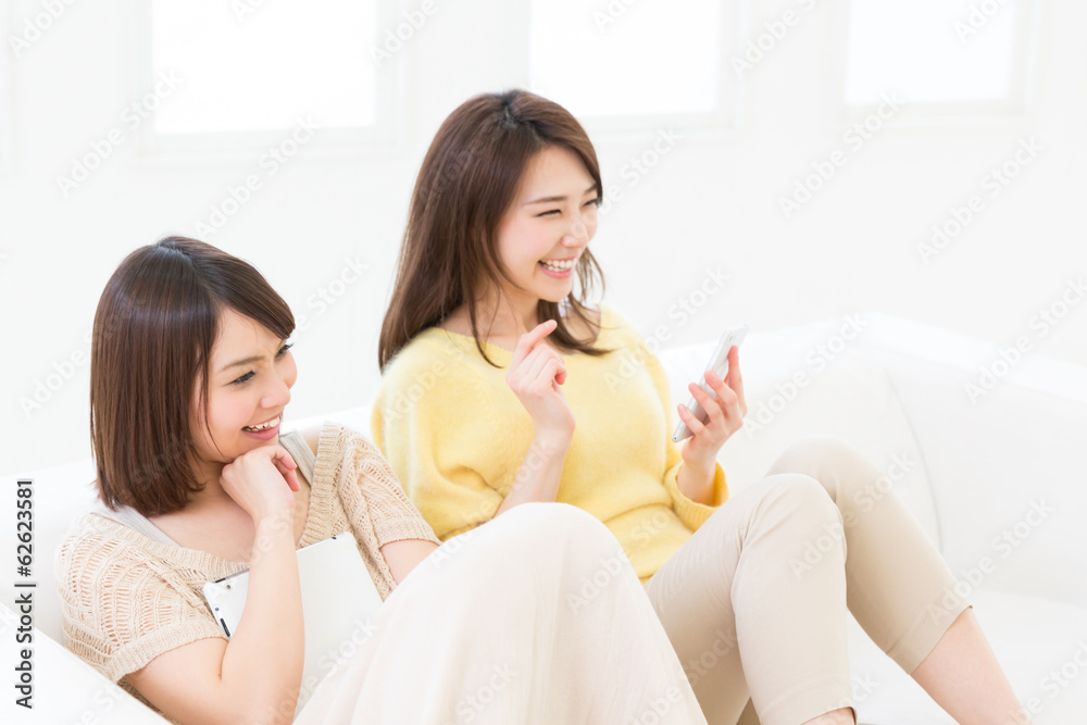 部屋でスマートフォンとタブレットを見る二人の女性 部屋でスマートフォンとタブレットを見る二人の女性