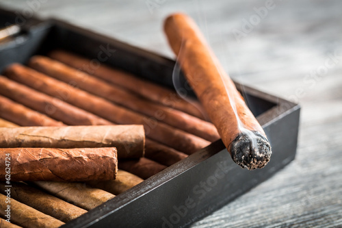 Burning cigar with smoke on wooden humidor © shaiith