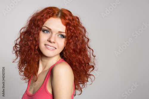 Smiling young woman with red hair on gray