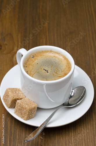 cup of black coffee with foam and cane sugar cubes, close-up