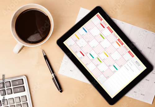 Tablet pc showing calendar on screen with a cup of coffee on a d