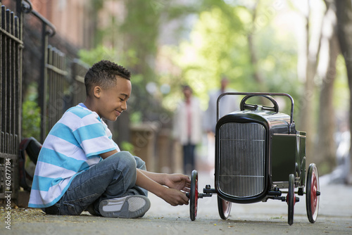 A Young Boy Playing With A Old Fashioned Toy Car On Wheels On A City Street.  photo