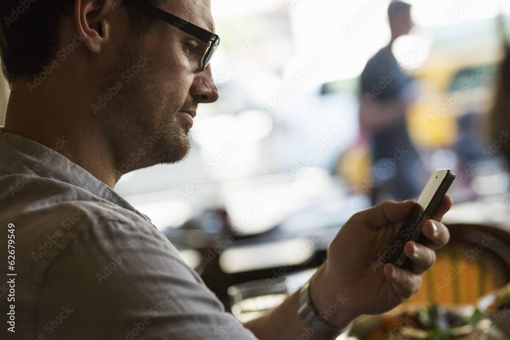 Business On The Go. A Man Sitting At A Cafe Table, Using His Mobile Phone. Looking Down At The Screen. Business On The Go. A Man Sitting At A Cafe Table, Using His Mobile Phone. Looking Down At The Screen.