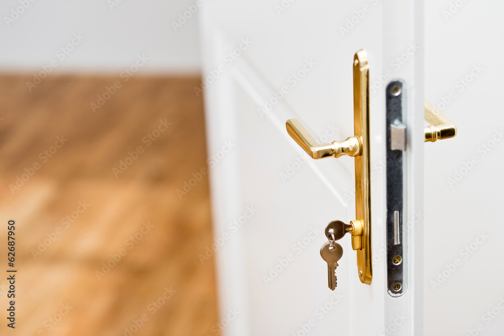 Keys in the keyhole with beautiful golden doorknob on white door