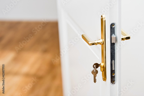 Keys in the keyhole with beautiful golden doorknob on white door photo