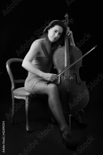 Beautiful brunette playing cello with selective light in red dre