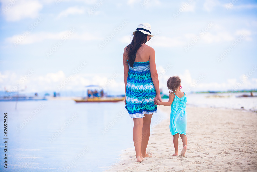 Back view of mother and her little daughter walking by the sea