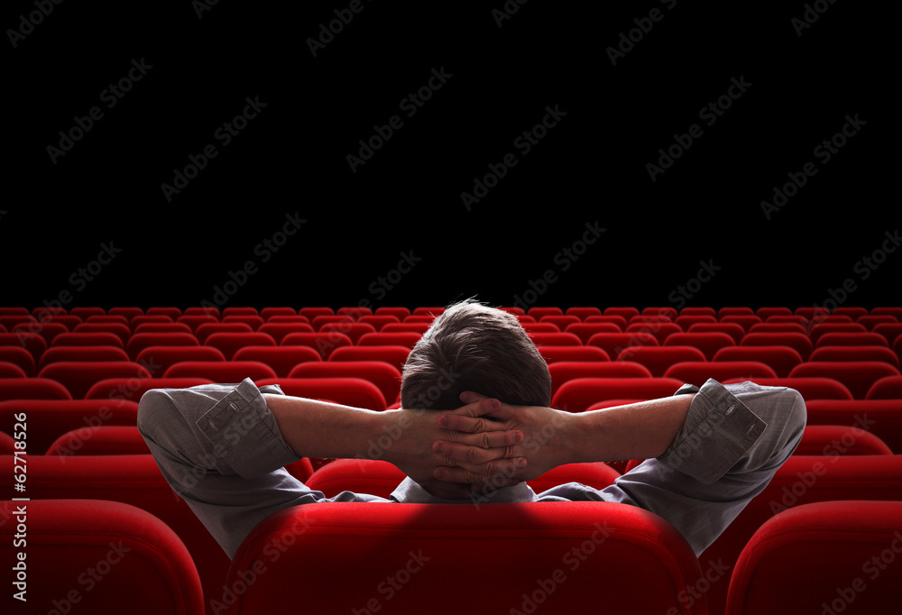 one man sitting in empty cinema or theater auditorium - obrazy, fototapety, plakaty 