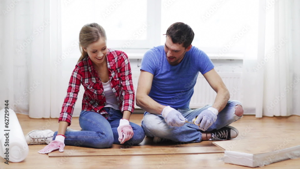 smiling couple measuring wood flooring