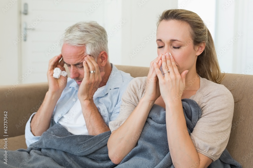 Sick couple sitting on the couch under a blanket Sick couple sitting on the couch under a blanket