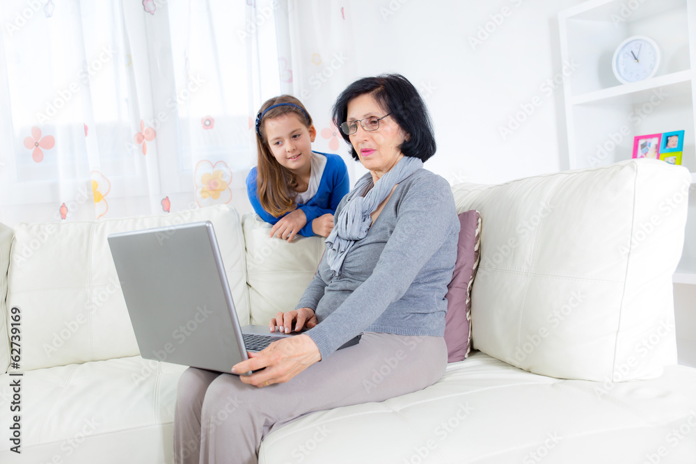 Cheerful little girl and her grandmother using a laptop at home Cheerful little girl and her grandmother using a laptop at home