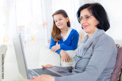 Cheerful little girl and her grandmother using a laptop at home