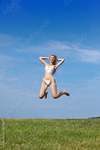 happy woman jumps in summer green field against blue sky..