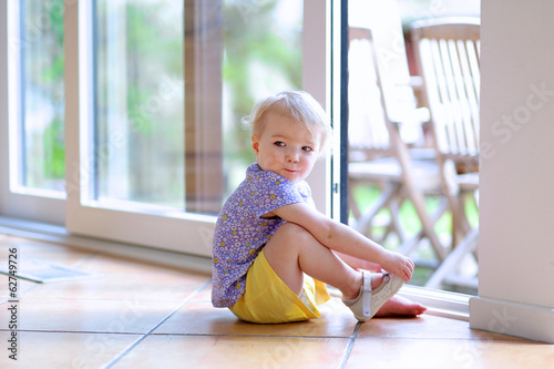 Cute toddler girl putting on her shoe sitting next to a window