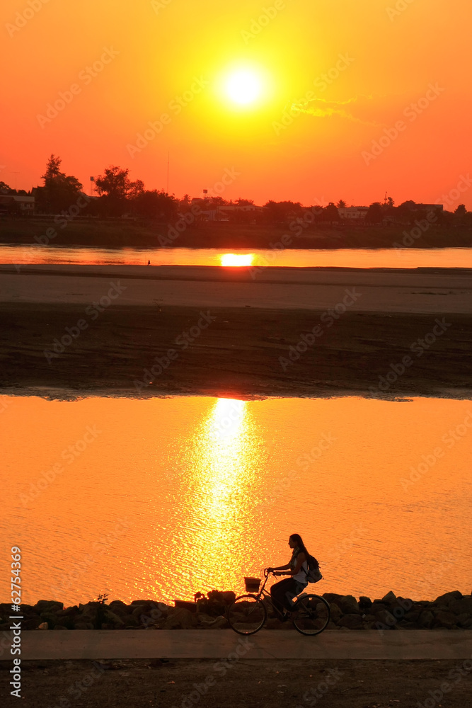 Silhouetted woman riding at Mekong river waterfront at sunset, V