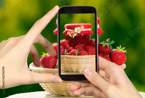 Man is taking photo of strawberries and jar