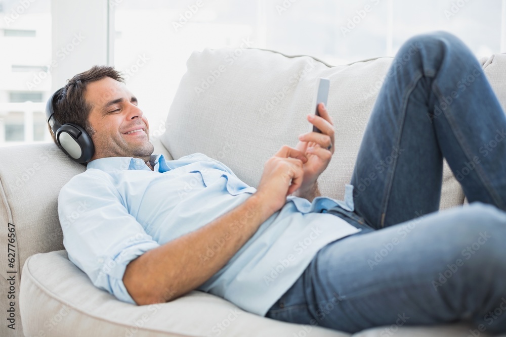 Happy handsome man lying on sofa using tablet and listening to Happy handsome man lying on sofa using tablet and listening to