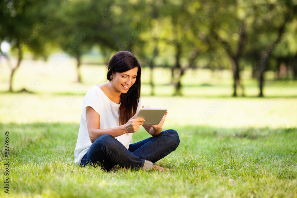 Happy young woman with digital tablet sitting on grass in park Happy young woman with digital tablet sitting on grass in park