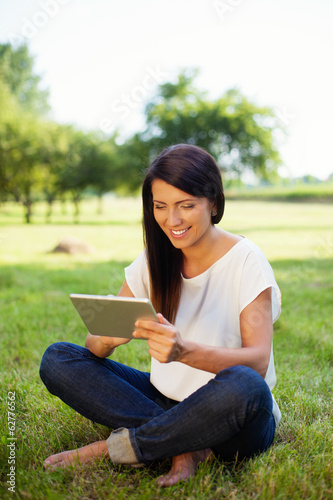 Happy woman using digital tablet in park, sitting on grass